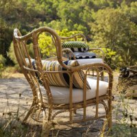 A patio with a rattan armchair with a white seat cushion and an extra striped cushion for lumbar support.