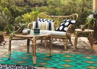 A patio with sofa and table made of rattan and a colorful rug with batik pattern.