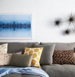 A photographic print by Daniel Håkansson hangs alongside a metal wall sculpture by by C. Jeré above colorful and richly textured pillows on the sectional.